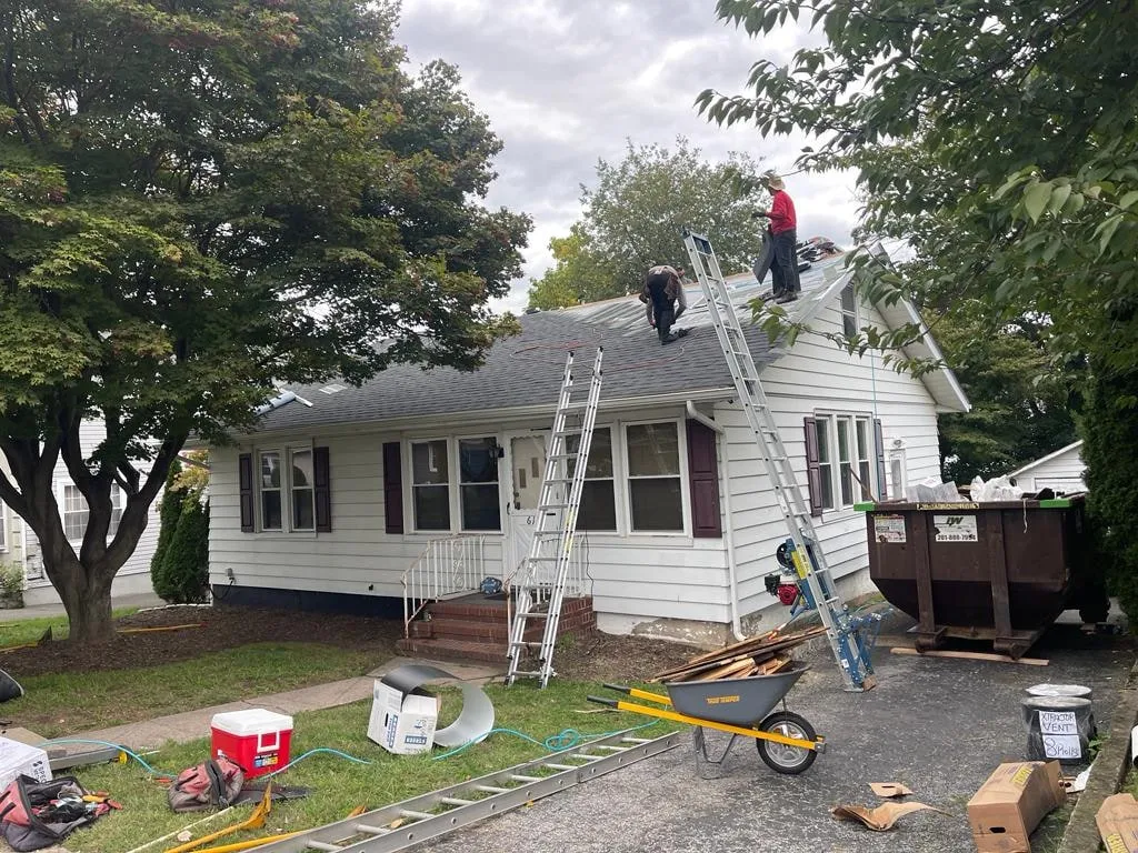 Crew re-roofing a white ranch home with a dumpster staged in the driveway