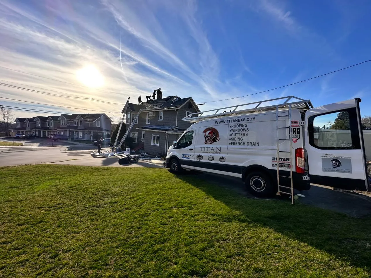 Titan Exterior Solutions van parked at a roofing job site with the crew on the roof
